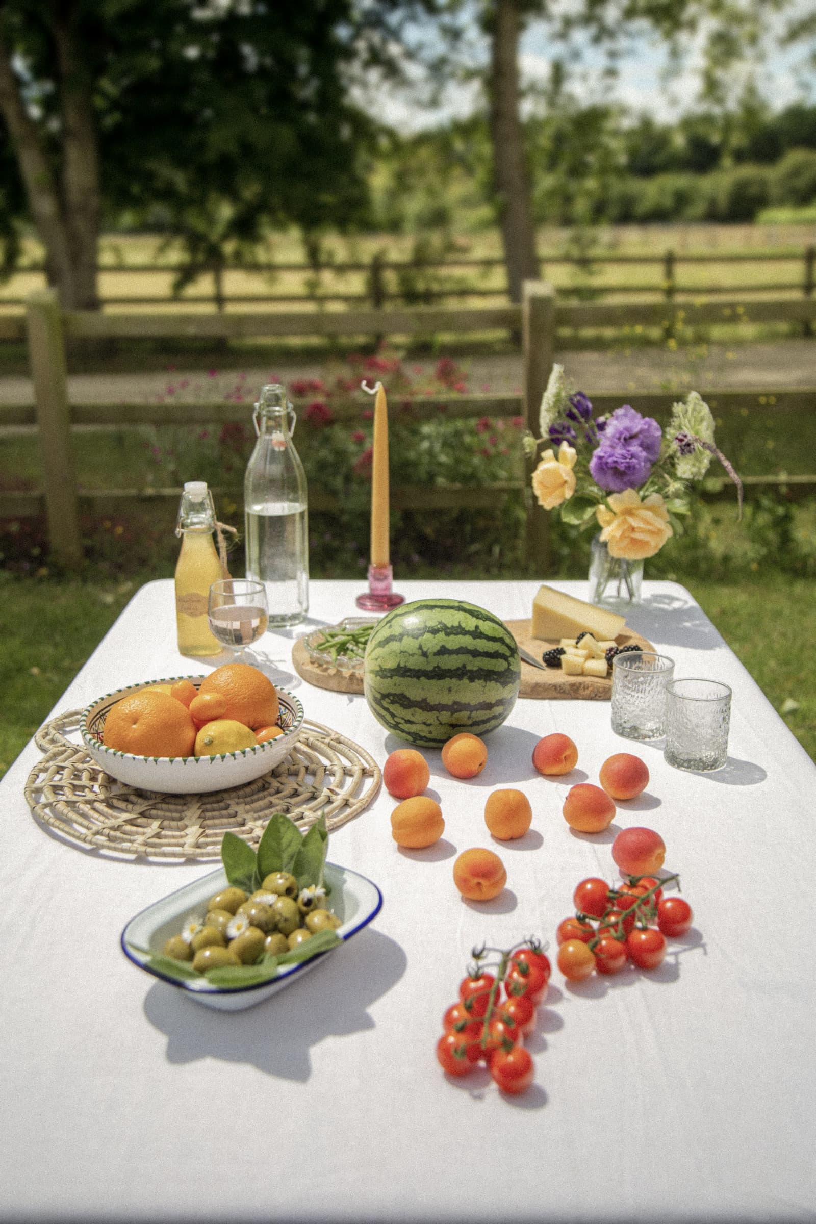 A garden table set with summer fruit, olives, and cut flowers