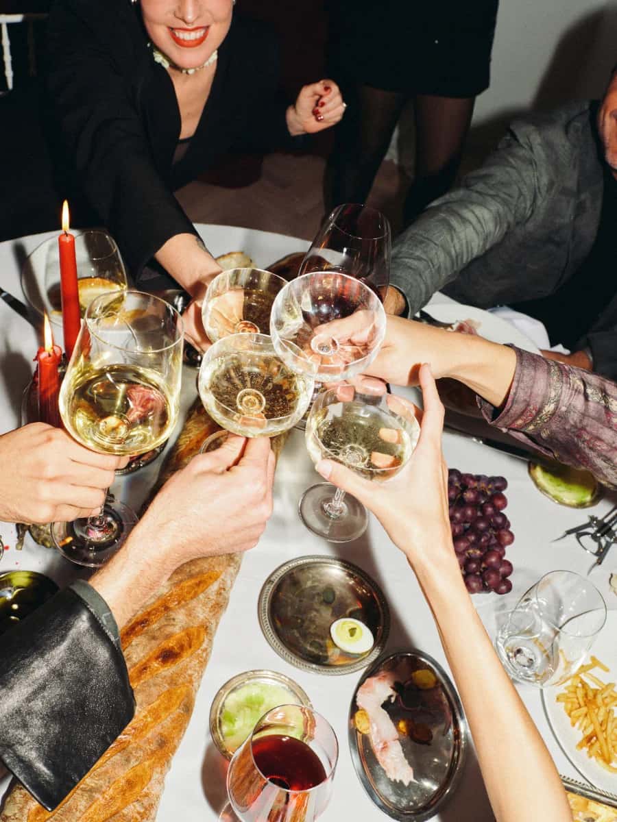 Friends reaching across a candlelit table to toast with wine glasses