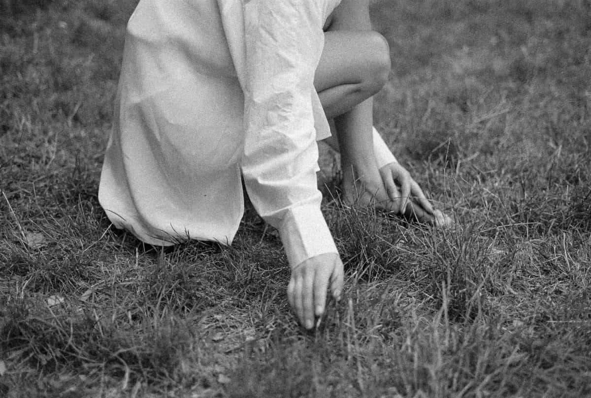 Kneeling in the grass in a white shirt, hands reaching into the garden beds